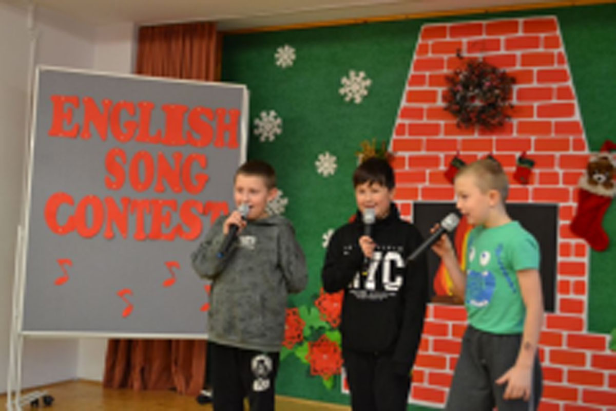 Uczniowie występują na scenie, trzymają mikrofony. Członkowie jury siedzą przy stoliku, wręczają dyplomy. Wspólne zdjęcie uczniów.