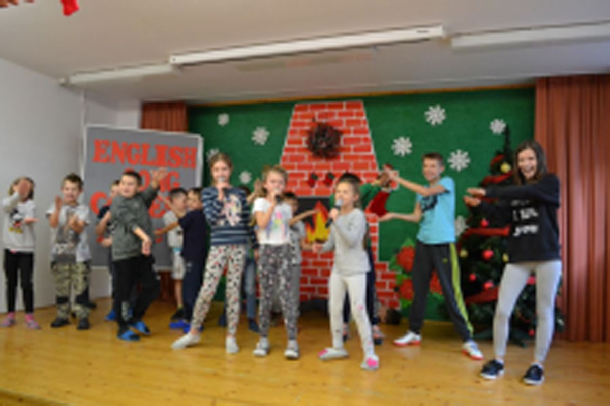 Uczniowie występują na scenie, trzymają mikrofony. Członkowie jury siedzą przy stoliku, wręczają dyplomy. Wspólne zdjęcie uczniów.