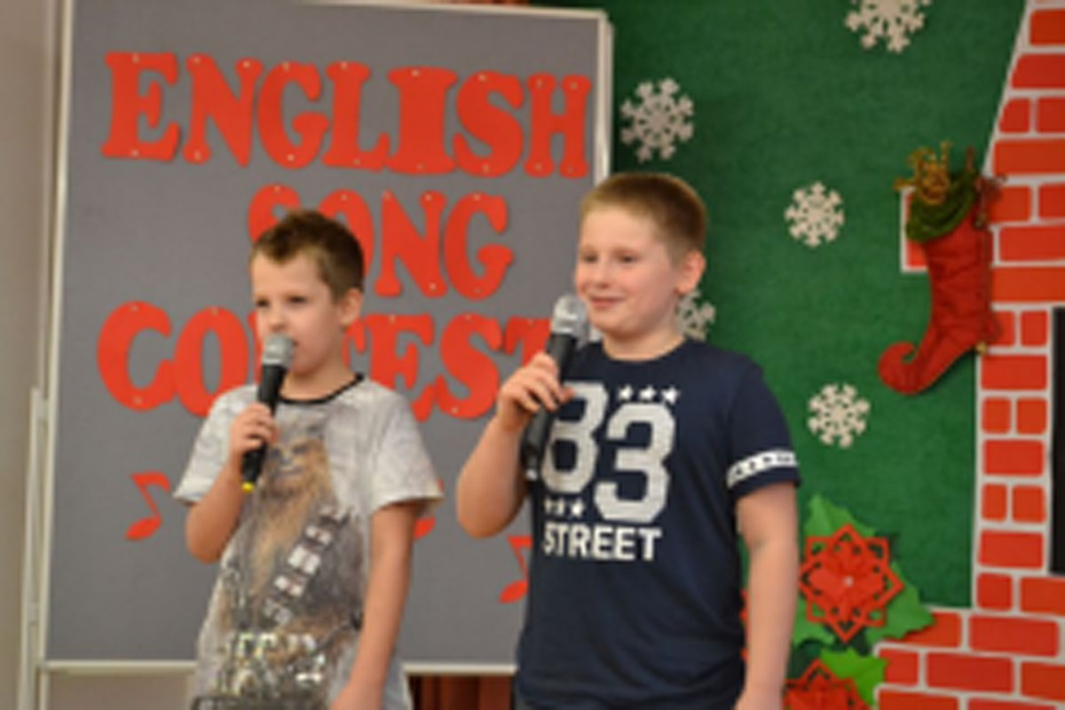 Uczniowie występują na scenie, trzymają mikrofony. Członkowie jury siedzą przy stoliku, wręczają dyplomy. Wspólne zdjęcie uczniów.