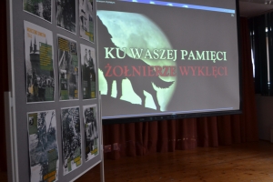 Zdjęcia przedstawiają salę, w której siedzą  uczniowie szkoły i oglądają prezentację.  Z frontu wystawione są stelaże, na których przypięte są zdjęcia przedstawiające Żołnierzy Wyklętych. Dyrektor szkoły i nauczycielka wręczają dyplomy uczniom.