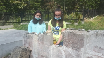 Uczniowie przy nagrobkach zapalają znicze.