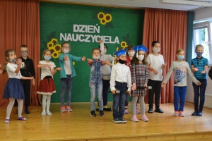 Uczniowie na scenie mówią do mikrofonu. Dyrektor mianuje pierwszoklasistów dużym ołówkiem.