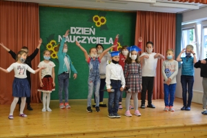 Uczniowie na scenie mówią do mikrofonu. Dyrektor mianuje pierwszoklasistów dużym ołówkiem.