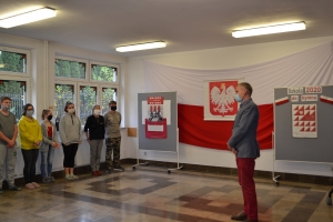 Na tle tablicy z biało-czerwonym sercem i napisem Serce dla Polski widoczna jest grupka dzieci w maseczkach. Jeden z chłopów ma uniesioną prawa rękę z palcami ułożonymi w znak zwycięstwa.ZSU Rabka