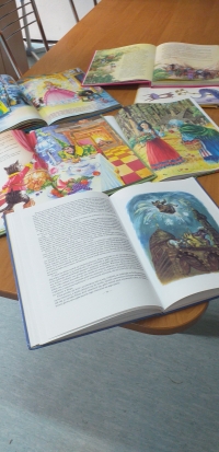 Grupa dzieci, przebranych w stroje bajkowych postaci  siedzą na dywanie i słuchają czytanej im bajki.