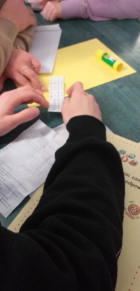 Uczniowie siedzą przy stolikach, rozwiązują rebusy, krzyżówki i wykreślanki, układają puzzle. Na stołach są ołówki, kleje, opakowania po jajkach niespodziankach, kartki w różnych kolorach. Uczniowie wykonują gazetkę z kart z zasadami bezpieczeństwa w siec