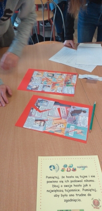 Uczniowie siedzą przy stolikach, rozwiązują rebusy, krzyżówki i wykreślanki, układają puzzle. Na stołach są ołówki, kleje, opakowania po jajkach niespodziankach, kartki w różnych kolorach. Uczniowie wykonują gazetkę z kart z zasadami bezpieczeństwa w siec