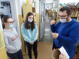 uczeń czyta informacje, dwie uczennice stoją obok