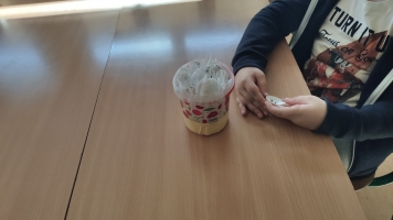 Uczniowie przy komputerach i stolikach. Układają wierze z plastikowych kubków, losują łyżeczki z zadaniami, grają w gry planszowe, rozwiązują zadania w programie komputerowym.