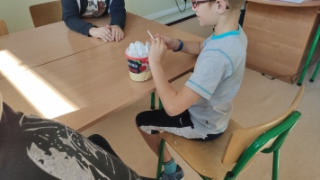 Uczniowie przy komputerach i stolikach. Układają wierze z plastikowych kubków, losują łyżeczki z zadaniami, grają w gry planszowe, rozwiązują zadania w programie komputerowym.