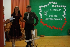 Uczniowie na scenie śpiewają pieśni. Koło sceny poczet sztandarowy, na scenie uczniowie przebrani w czarne stroje zaborców i  na biało za orła. Uczniowie składają znicze pod krzyżem.