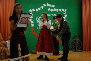 Uczniowie na scenie śpiewają pieśni. Koło sceny poczet sztandarowy, na scenie uczniowie przebrani w czarne stroje zaborców i  na biało za orła. Uczniowie składają znicze pod krzyżem.