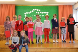 Uczniowie na scenie śpiewają pieśni. Koło sceny poczet sztandarowy, na scenie uczniowie przebrani w czarne stroje zaborców i  na biało za orła. Uczniowie składają znicze pod krzyżem.