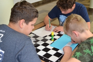 Uczniowie przy stolikach, rozwiązują krzyżówki, wykreślanki, rebusy.