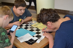 Uczniowie przy stolikach, rozwiązują krzyżówki, wykreślanki, rebusy.