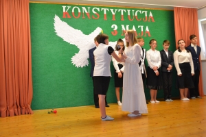 Uczniowie na scenie. Przebrani w stroje biało czarne i ułańskie z epoki. Tańczą, markują ruchy kopania, ogrzewania przy ognisku.