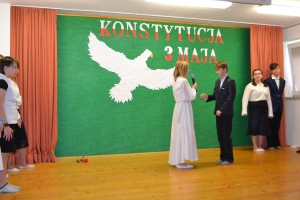 Uczniowie na scenie. Przebrani w stroje biało czarne i ułańskie z epoki. Tańczą, markują ruchy kopania, ogrzewania przy ognisku.