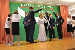 Uczniowie na scenie. Przebrani w stroje biało czarne i ułańskie z epoki. Tańczą, markują ruchy kopania, ogrzewania przy ognisku.