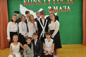 Uczniowie na scenie. Przebrani w stroje biało czarne i ułańskie z epoki. Tańczą, markują ruchy kopania, ogrzewania przy ognisku.