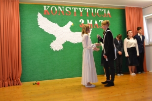 Uczniowie na scenie. Przebrani w stroje biało czarne i ułańskie z epoki. Tańczą, markują ruchy kopania, ogrzewania przy ognisku.