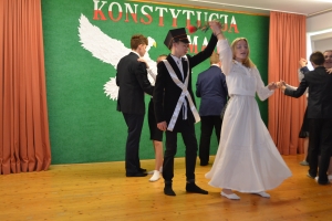 Uczniowie na scenie. Przebrani w stroje biało czarne i ułańskie z epoki. Tańczą, markują ruchy kopania, ogrzewania przy ognisku.