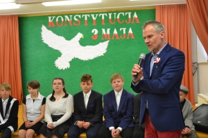 Uczniowie na scenie. Przebrani w stroje biało czarne i ułańskie z epoki. Tańczą, markują ruchy kopania, ogrzewania przy ognisku.