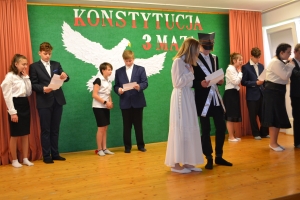 Uczniowie na scenie. Przebrani w stroje biało czarne i ułańskie z epoki. Tańczą, markują ruchy kopania, ogrzewania przy ognisku.