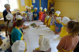 uczniowie ubrani w fartuszki jedzą chleb, oglądają film