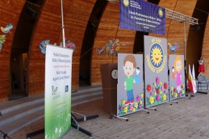 Występujący na scenie tańczą z pomponami, ze wstęgami. Na scenie dekoracja, pacynki Jacek i Agatka. Order Uśmiechu wręcza sekretarz Kapituły Orderu Uśmiechu i państwo Burcanowie.