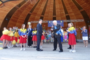 Występujący na scenie tańczą z pomponami, ze wstęgami. Na scenie dekoracja, pacynki Jacek i Agatka. Order Uśmiechu wręcza sekretarz Kapituły Orderu Uśmiechu i państwo Burcanowie.