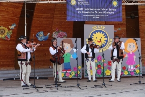 Występujący na scenie tańczą z pomponami, ze wstęgami. Na scenie dekoracja, pacynki Jacek i Agatka. Order Uśmiechu wręcza sekretarz Kapituły Orderu Uśmiechu i państwo Burcanowie.